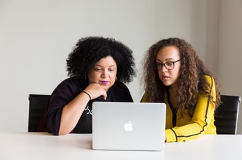Two women looking at the screen of a MacBook laptop.