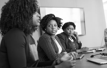 Three Black women sit at a conference table together during a meeting.
