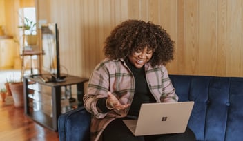 Black woman sitting on a couch on her computer, smiling. 