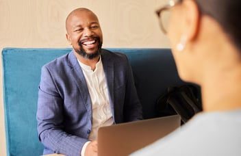 Black professional man laughing over an open laptop while sitting across from a woman at an office
