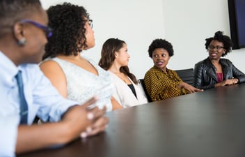 Five diverse employees speak with one another in a group meeting.