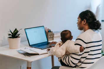 A mother works from home with a child in her lap.