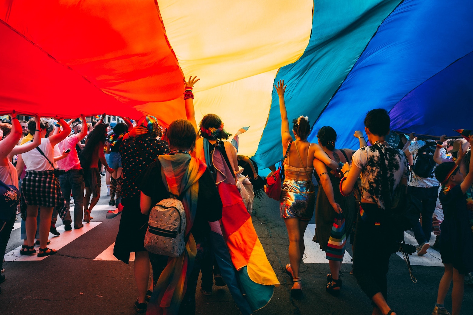 Parade goers collectively hold up a giant rainbow flag in honor of Pride Month.