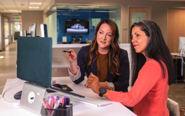 Two women sitting together at a desk, looking at a laptop screen.