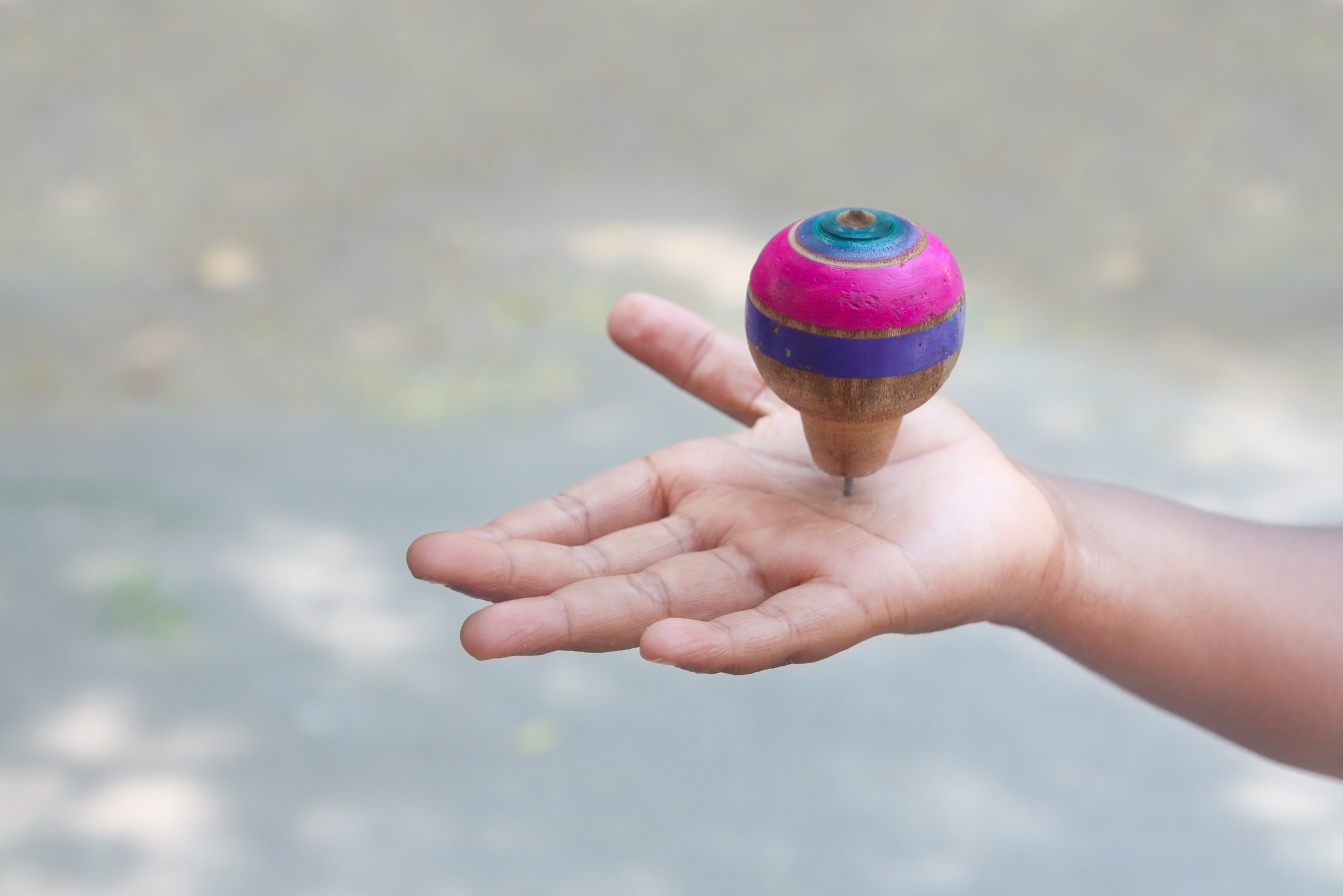 Colorful wooden top resting on its point in the hand of a child with light brown skin 